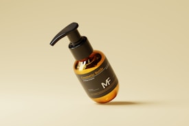 A sleek, amber-colored cosmetic bottle with a black pump lid, labeled 'Cosmetic Bottle' and 'MF', is centrally placed against a minimalist, light tan background. The bottle has a modern design and is slightly tilted, creating a dynamic visual effect.