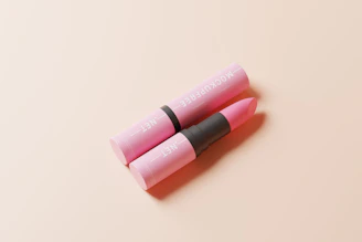 A close-up of a luxurious blush pink lipstick with a rose gold tube, resting on soft ivory fabric.