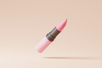 A pink lipstick with a black middle section is depicted against a beige background. The lipstick appears suspended in mid-air with a shadow cast below it.