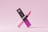 A pink lipstick is positioned in an elegant manner along with its packaging. The lipstick tube is sleek and modern, with a gradient of pink shades transitioning from light at the bottom to a darker hue at the top. The packaging displays the brand logo along with text in a matching pink color scheme. The overall aesthetic is minimalist and chic, set against a light pink background.