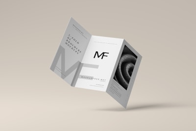 A tri-fold brochure mockup is depicted with a minimalist design. It features clean lines and a modern aesthetic with a grayscale color scheme. The front side has an 'MF' logo, and there's an abstract spiral image on one of the panels.