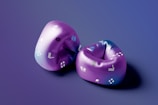 Two purple inflatable swimming sleeves with various small graphics, including flippers, life buoys, and waves, placed on a surface with a smooth gradient background transitioning from a deep purple to blue.