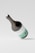 A large wine bottle mockup with a sleek design, featuring minimalistic white and mint green labeling. The bottle is tilted at an angle against a light gray background, casting a soft shadow on the surface.