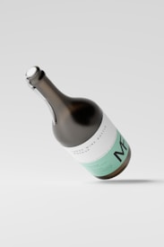 A large wine bottle mockup with a sleek design, featuring minimalistic white and mint green labeling. The bottle is tilted at an angle against a light gray background, casting a soft shadow on the surface.