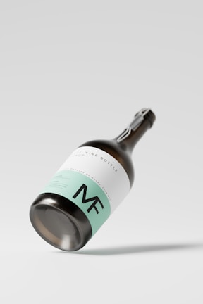A sleek wine bottle featuring a minimalist design, with a mint green and white label, prominently displaying the initials 'MF'. The bottle is positioned at an angle against a plain, light background, casting a subtle shadow.