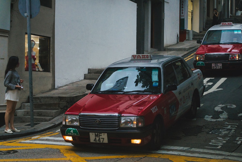 a red taxi cab driving down a street next to a woman