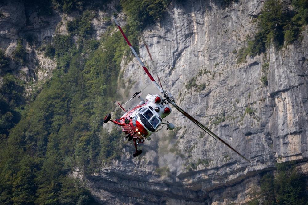 a red and white helicopter flying over a mountain