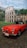 A smiling man standing beside a classic red Alfa Romeo on a sunlit Italian coastal road.