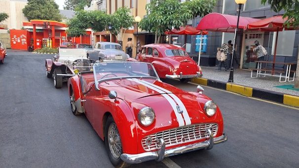 Classic American cars parked near a festive outdoor market showcasing local and American foods.