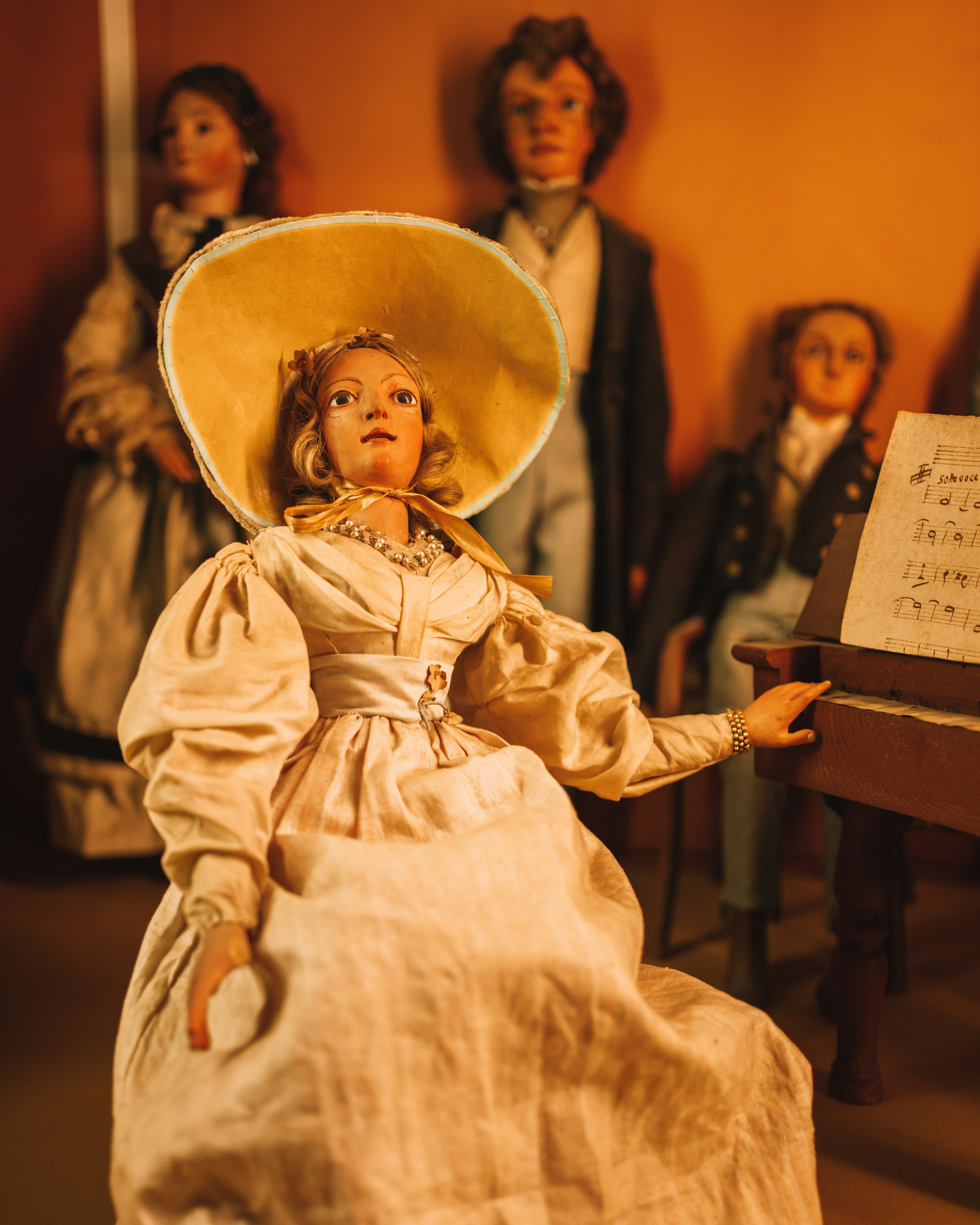 a doll with a large hat on her head sitting in front of a piano