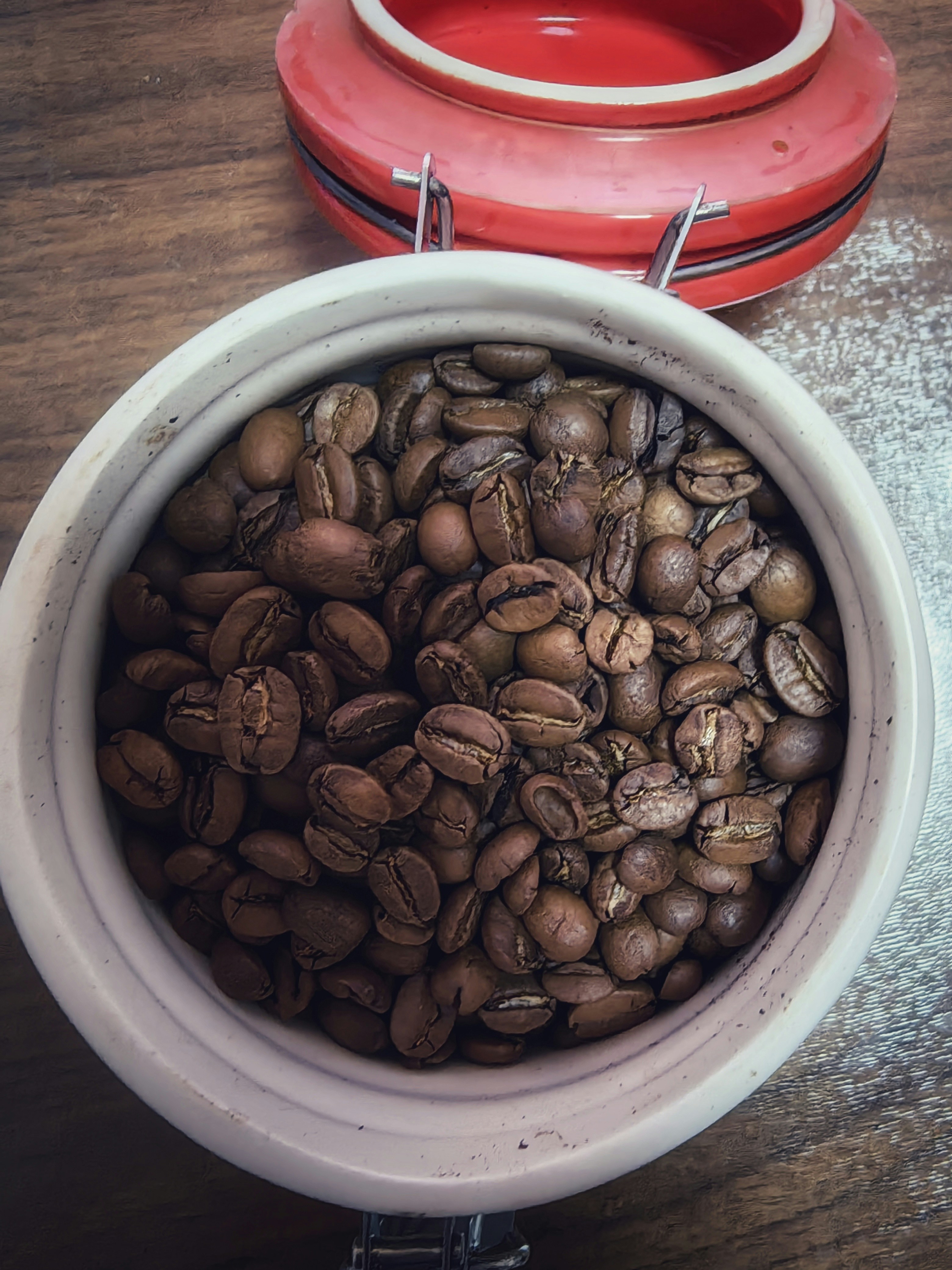 Coffee roaster pouring fresh beans into a ceramic cup on a warm wooden counter, soft morning light
