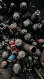 A collection of old, rusted mechanical parts, including various-sized nuts, bolts, and cylindrical components, all covered in dust and grime. The mix of colors and metal textures suggests an industrial or workshop setting.