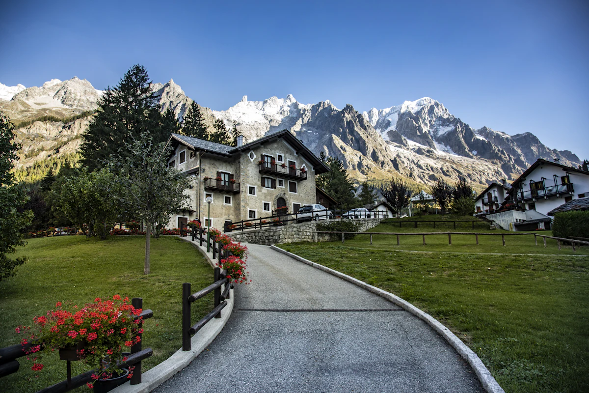 A large chalet and a lawn in Courmayeur below a row of jagged snowy peaks