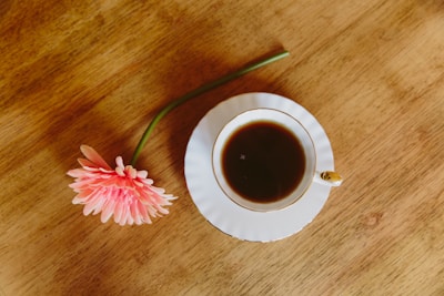 A serene coffee cup beside a pink flower on a white tabletop.