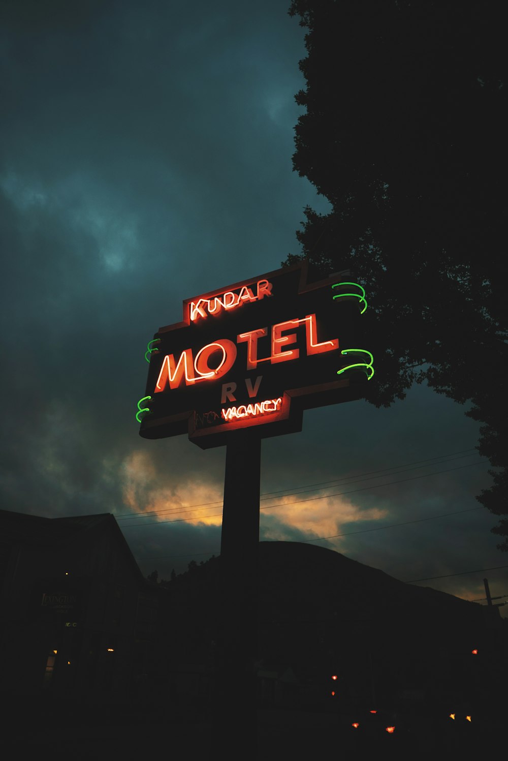 a motel sign lit up at night under a cloudy sky