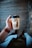 A hand holding a cup of Cowboy Coffee Co. against a wooden background. The person is wearing a watch with a brown strap and a light blue shirt.
