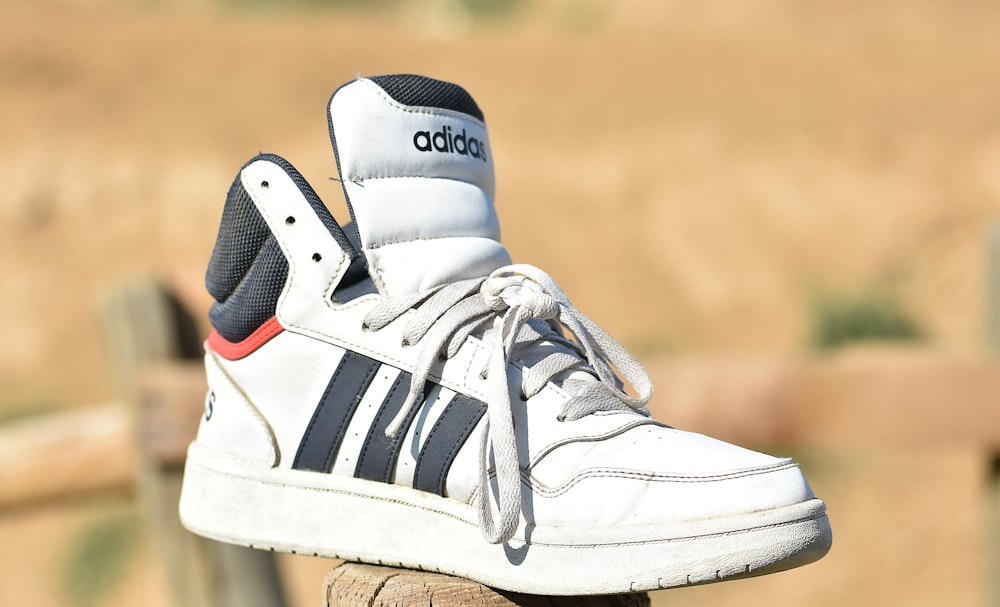 a pair of white adidas sneakers sitting on top of a wooden post