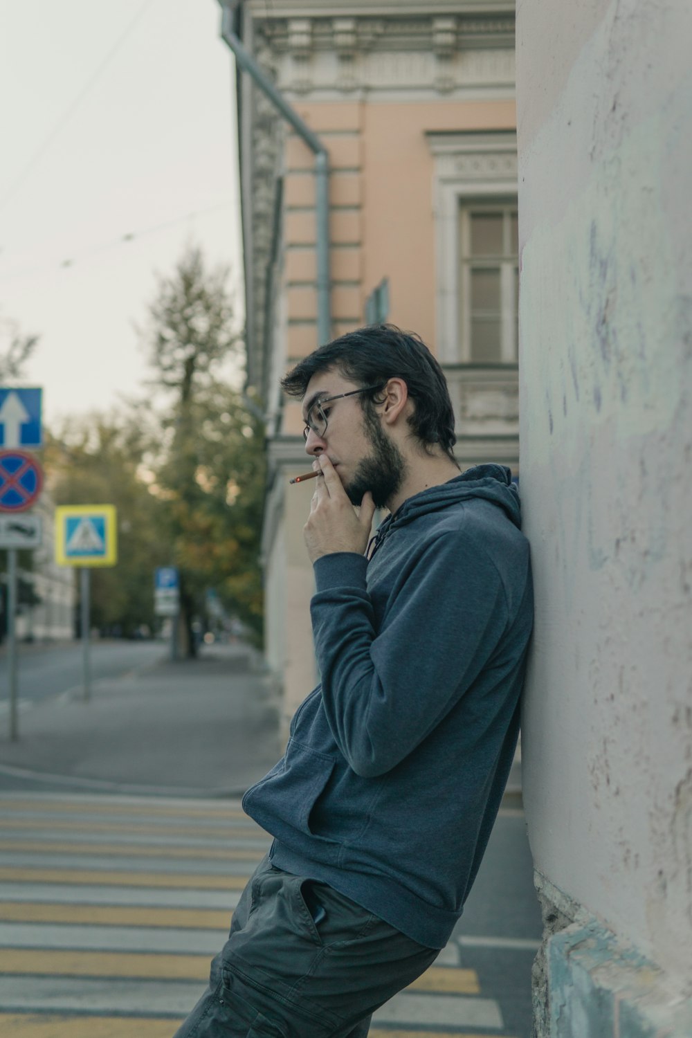 a man leaning against a wall smoking a cigarette