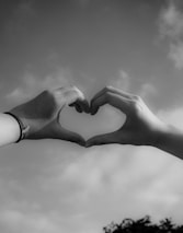 Close-up of hands forming a heart shape against a bright sky.