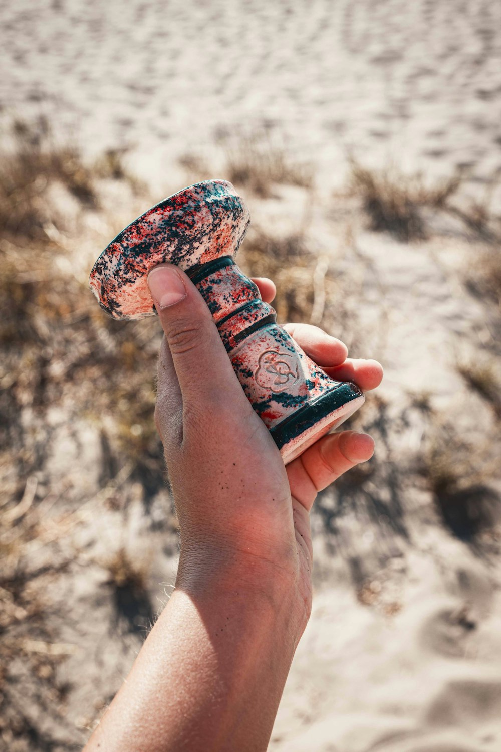 a hand holding a bottle in the sand