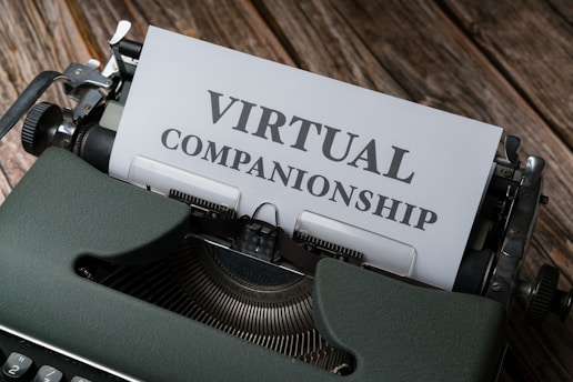 An old-fashioned typewriter with the words 'Virtual Companionship' typed on a sheet of paper. The image includes a green typewriter and a wooden surface background.