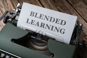 A vintage typewriter with an olive green body is set on a wooden surface, with a sheet of paper inserted that reads 'BLENDED LEARNING' in bold, capital letters.