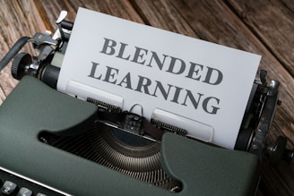 A vintage typewriter with an olive green body is set on a wooden surface, with a sheet of paper inserted that reads 'BLENDED LEARNING' in bold, capital letters.