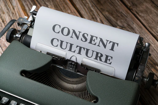 A vintage typewriter with a sheet of paper inserted, displaying the words 'CONSENT CULTURE' in large, bold letters. The typewriter is set on a wooden surface, creating a rustic and nostalgic atmosphere.