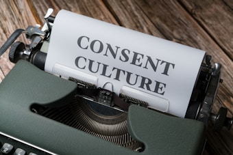 A vintage typewriter with a sheet of paper inserted, displaying the words 'CONSENT CULTURE' in large, bold letters. The typewriter is set on a wooden surface, creating a rustic and nostalgic atmosphere.