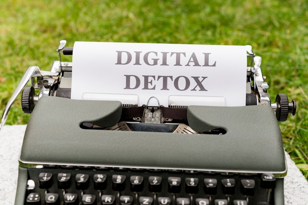 A vintage typewriter with a sheet of paper displaying the text 'DIGITAL DETOX' set against a backdrop of green grass.