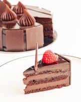 A decadent chocolate cake slice topped with raspberries and a drizzle of sauce.