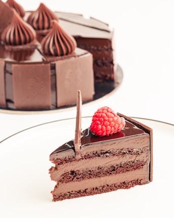 A close-up of a rich chocolate cake with glossy ganache and fresh raspberries on top.