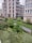 A modern urban apartment complex with multiple stories and balconies overlooks a well-maintained garden area. The garden is lush with a variety of plants and bushes, creating an inviting green space. A paved pathway runs through the greenery, and there is a street lamp near the path. The buildings are mostly neutral in color, contrasting with the vibrant garden.