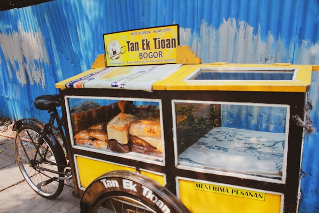 A colorful bicycle parked by a sunny North Shore beach, stacked with freshly baked banana bread loaves.