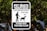 A black and white sign with text warning about pet waste transmitting disease. It instructs pet owners to leash and clean up after their pets. The sign features an illustration of a person walking a dog. It is mounted on a post surrounded by trees.