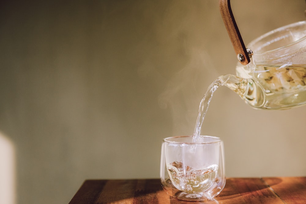 a pitcher pouring water into a glass on top of a wooden table