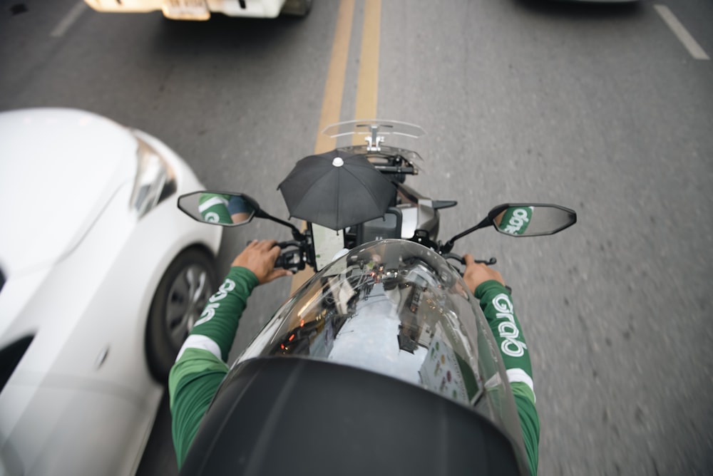 a man riding a motorcycle down a street next to a white car