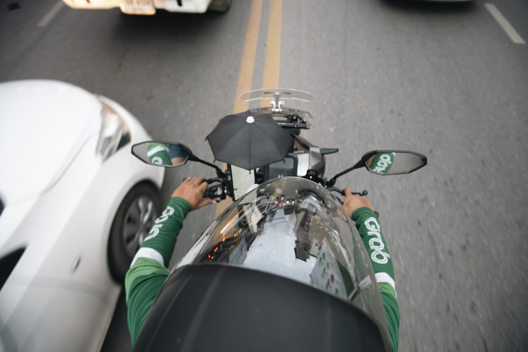 a man riding a motorcycle down a street next to a white car,