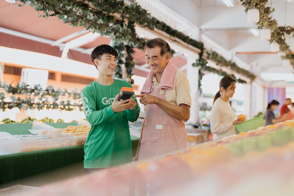 two men standing next to each other looking at a cell phone