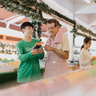 two men standing next to each other looking at a cell phone