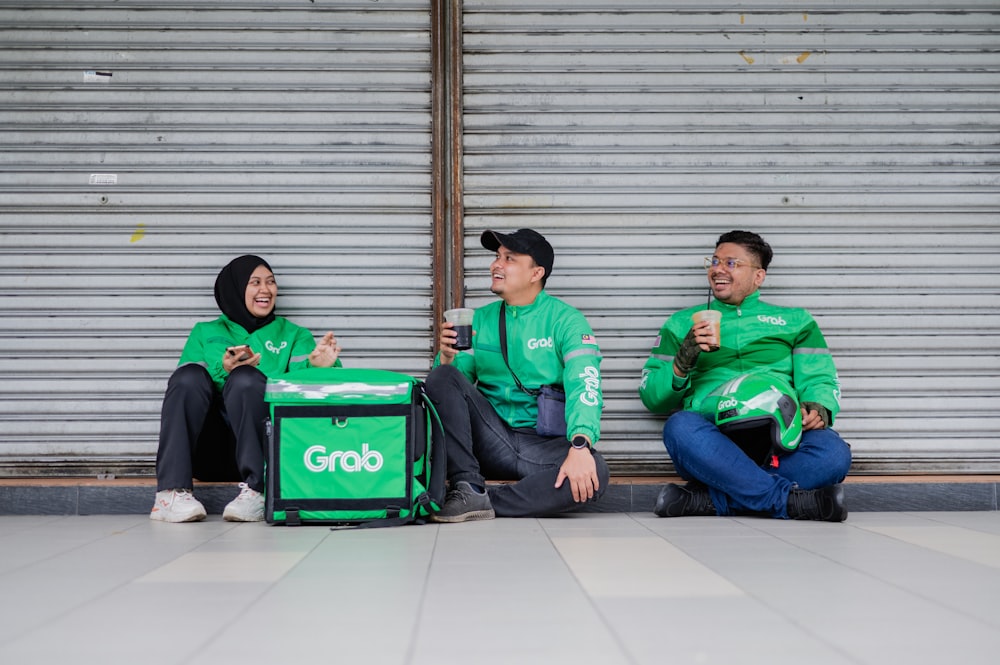 three people in green shirts sitting on the ground