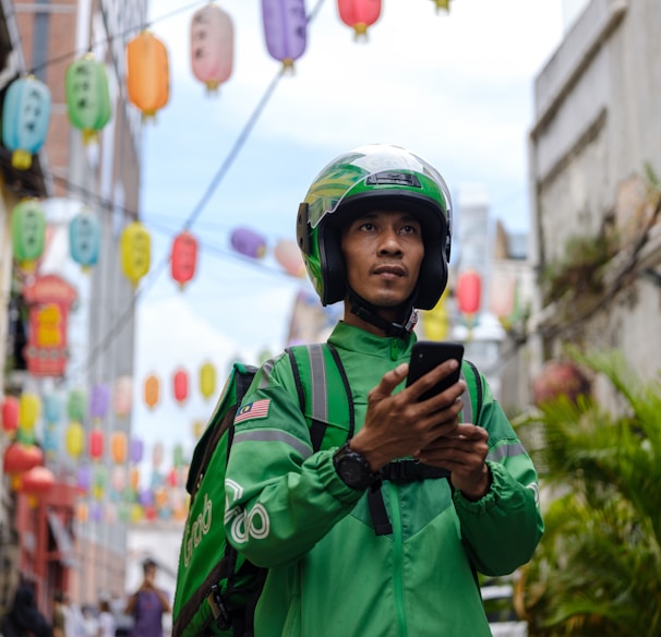 a man in a green jacket and helmet looking at a cell phone