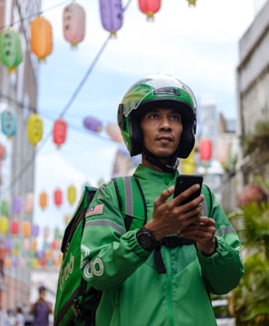 a man in a green jacket and helmet looking at a cell phone