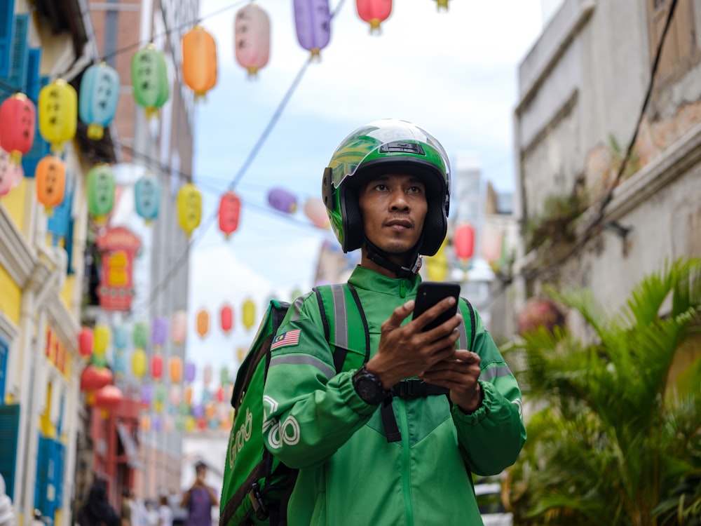 a man in a green jacket and helmet looking at a cell phone