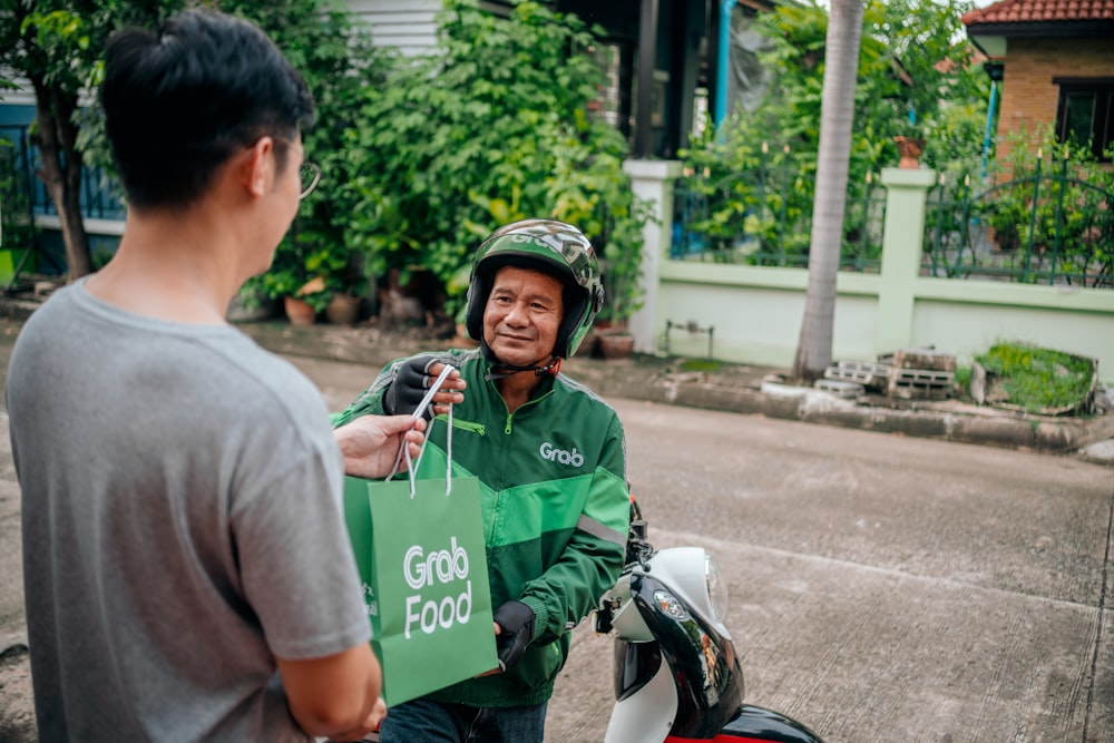a man holding a green bag standing next to a man on a scooter