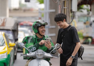 a man in a green jacket on a motor scooter looking at a cell