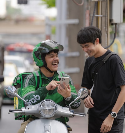 a man in a green jacket on a motor scooter looking at a cell