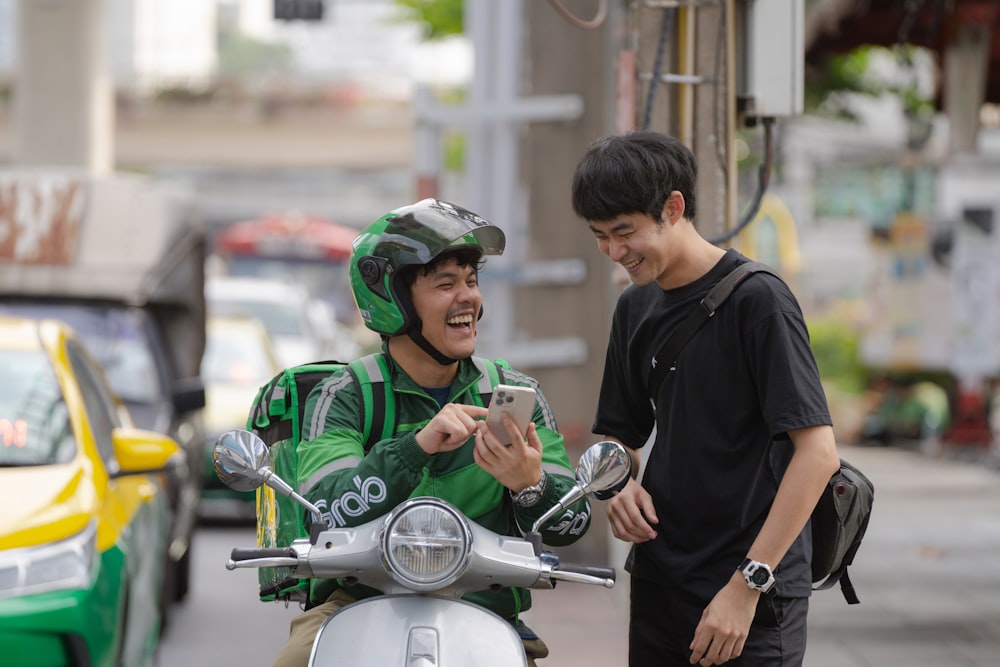 a man in a green jacket on a motor scooter looking at a cell