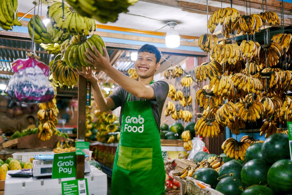 Ein Mann in einer Schürze hält ein Bündel Bananen in der Hand