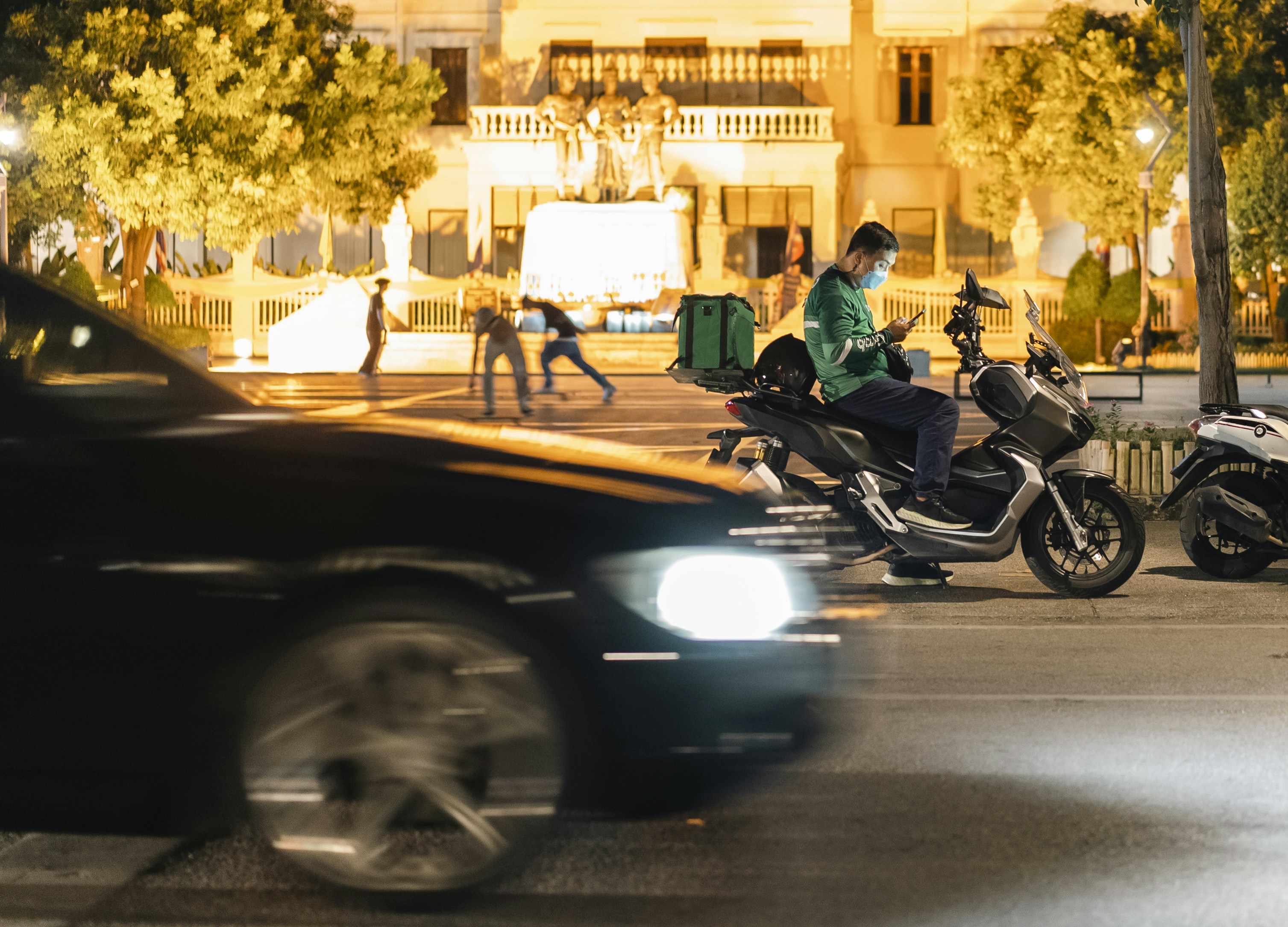 a man riding a motorcycle down a street next to a car, 